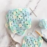 Three finished granny squares and one unfinished with a crochet hook in the piece.