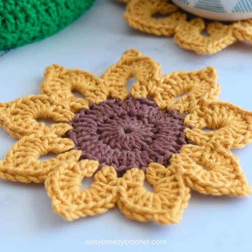 Crochet sunflower coaster in gold and brown yarn.