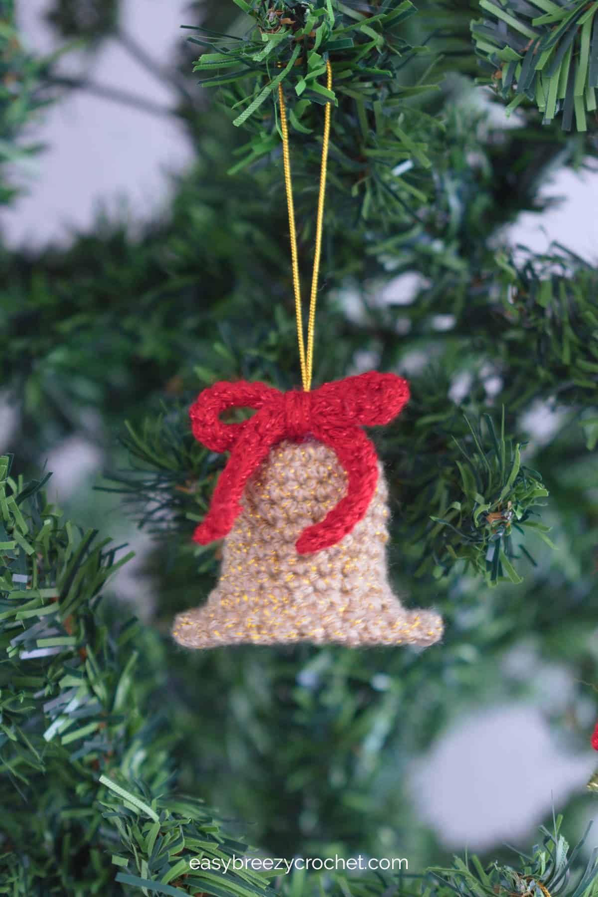 A gold crochet bell ornament with a red bow.