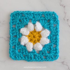 A blue granny square with a white popcorn stitch flower.