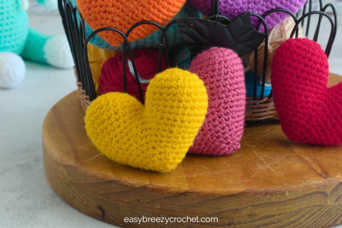 Yellow, pink and red crochet hearts on a wooden block.
