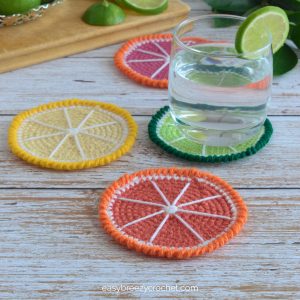 Crochet citrus coasters on a table with a glass of water.