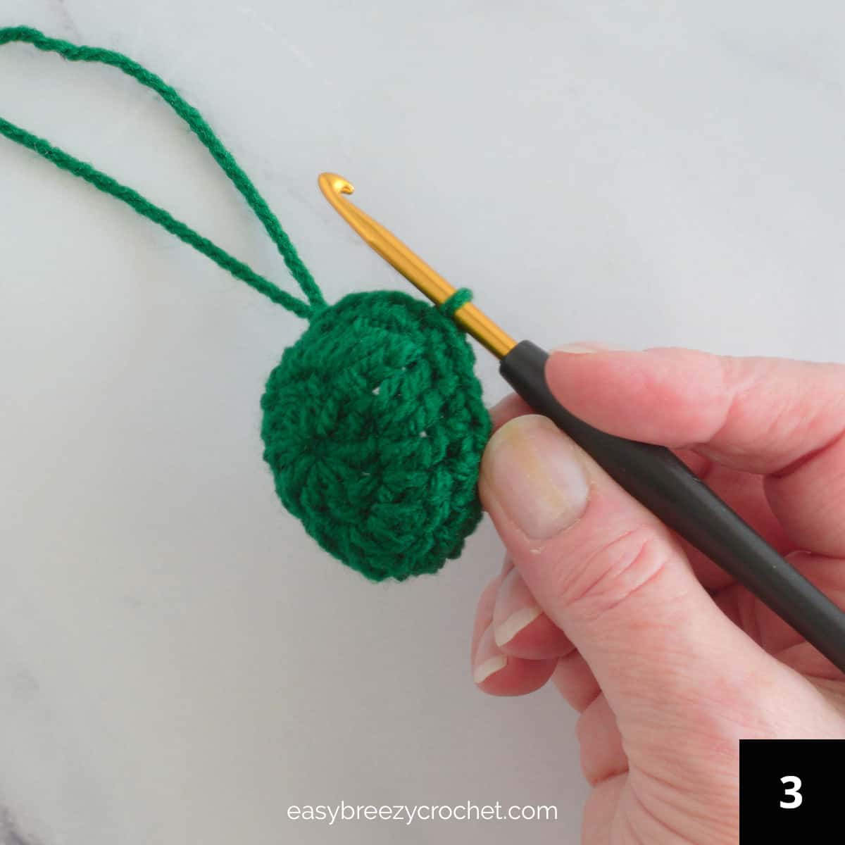 A hand holding a crochet hook and a green crocheted circle.
