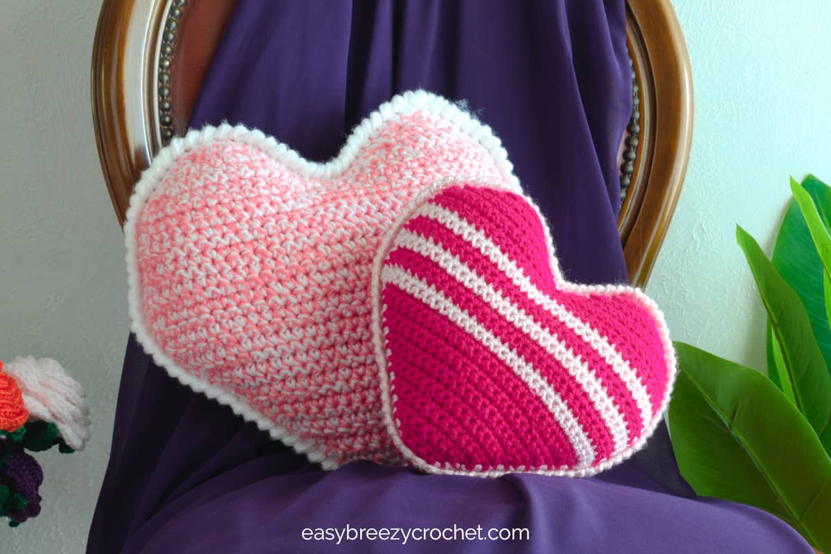 Two heart shaped crochet pillows on a chair.