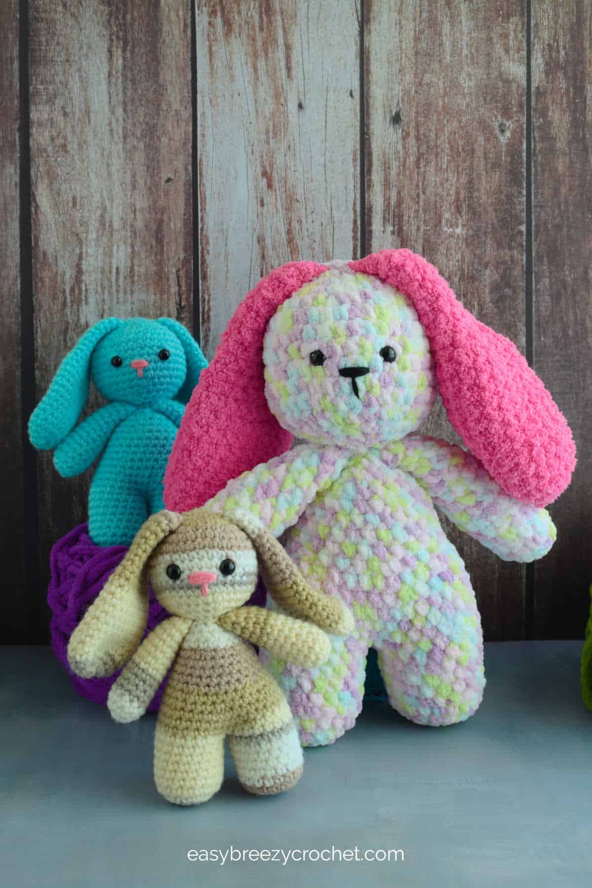 A large crochet bunny with hot pink ears, and two smaller crochet bunnies.