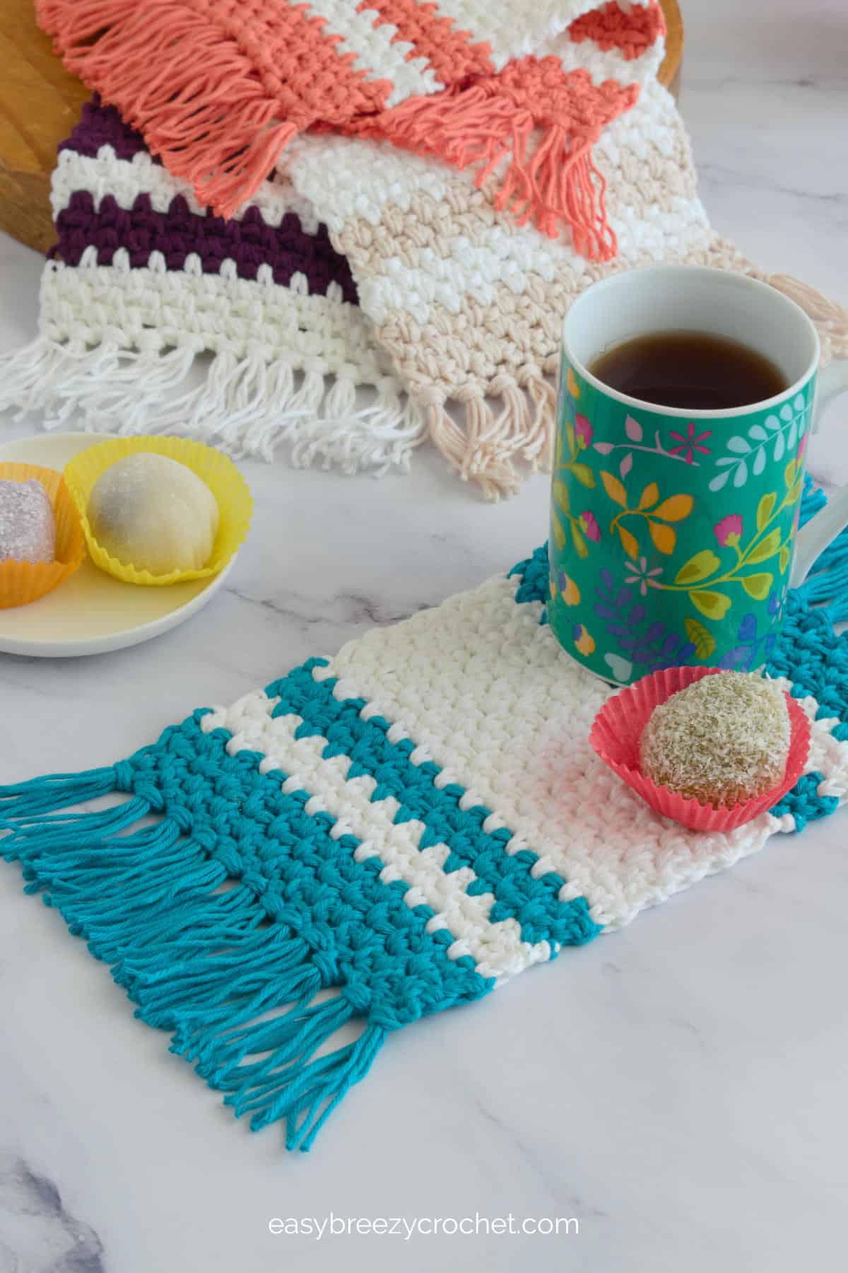 A blue and white mug rug with a coffee mug and several different colored mug rugs in the background.
