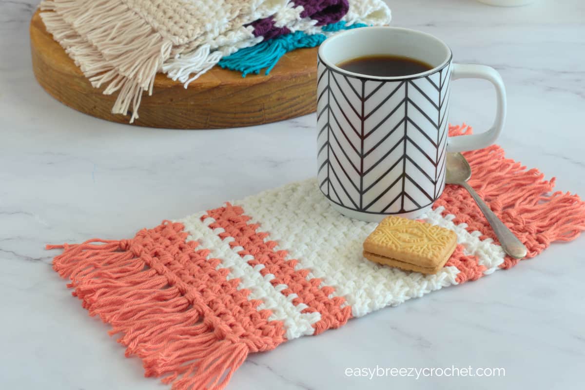 An orange and white mug rug with a coffee mug and a cookie.