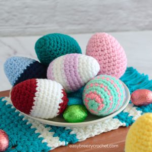 Crochet Easter eggs on a plate with mini chocolate eggs.