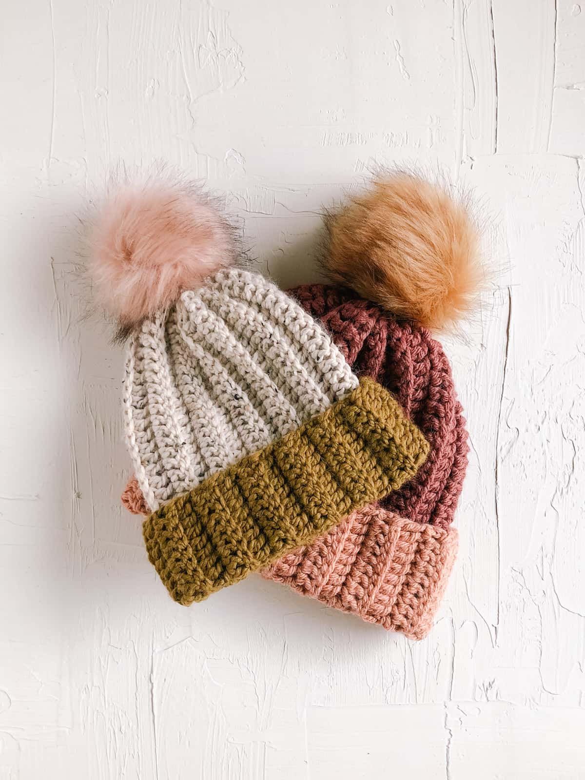 Two crochet beanies with fur pom poms.