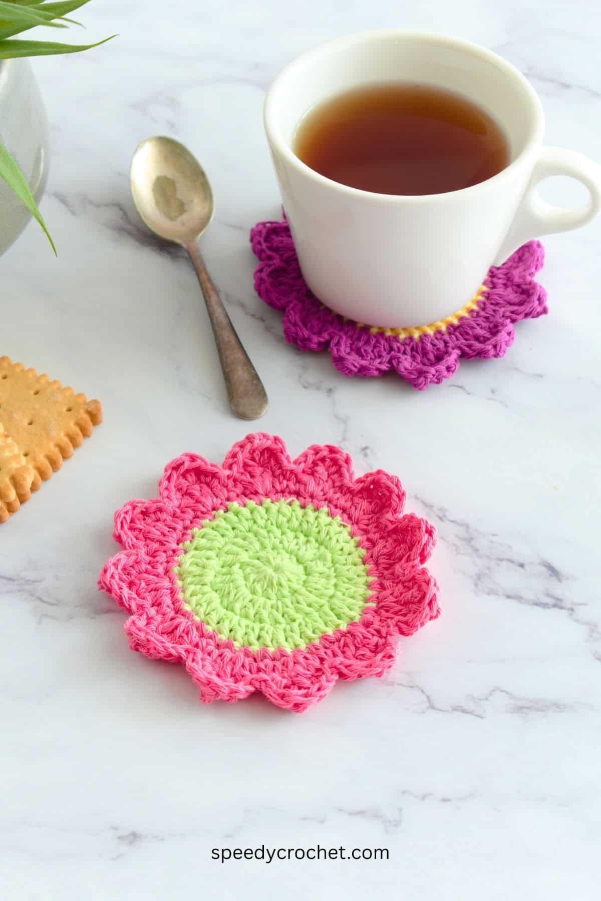 A green and pink crochet flower coaster.