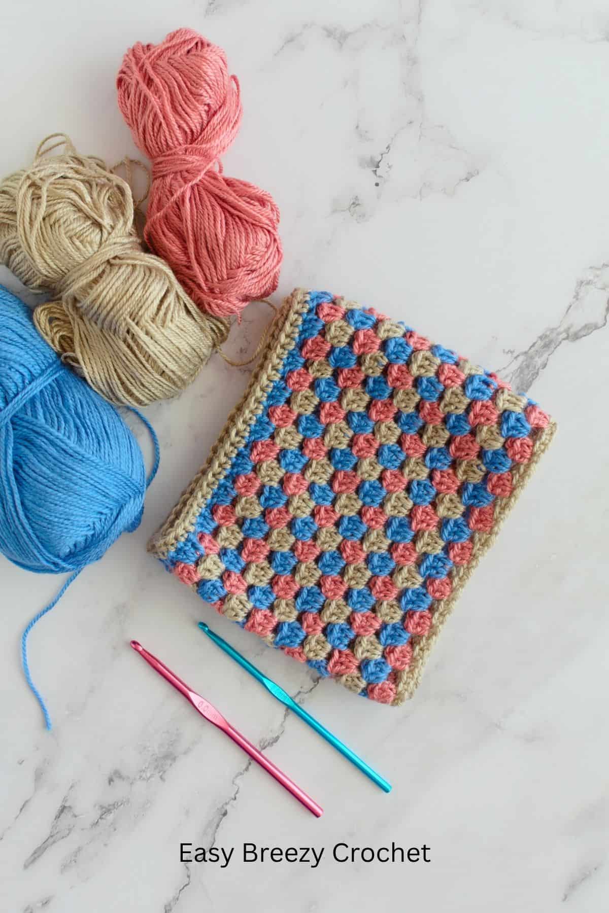 A crochet cowl on a table with balls of yarn and crochet hooks.