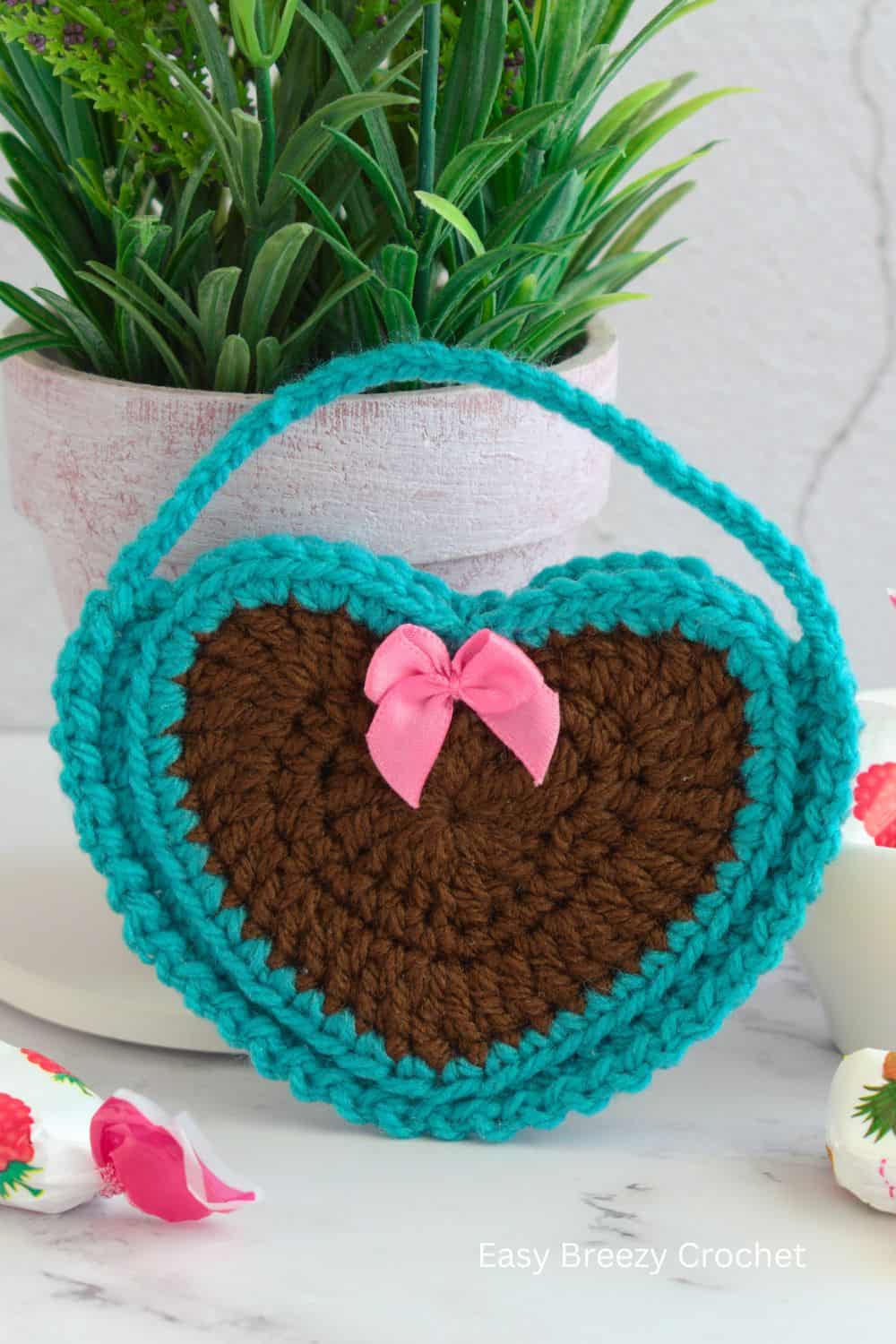 Brown and blue crochet heart bag with a pink ribbon.