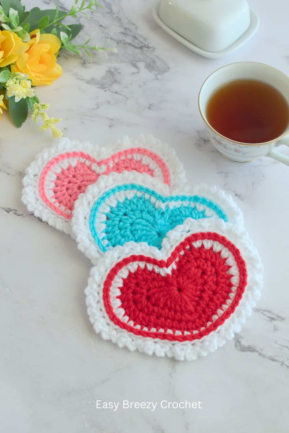 Pink, blue and red crochet heart coasters on a table.