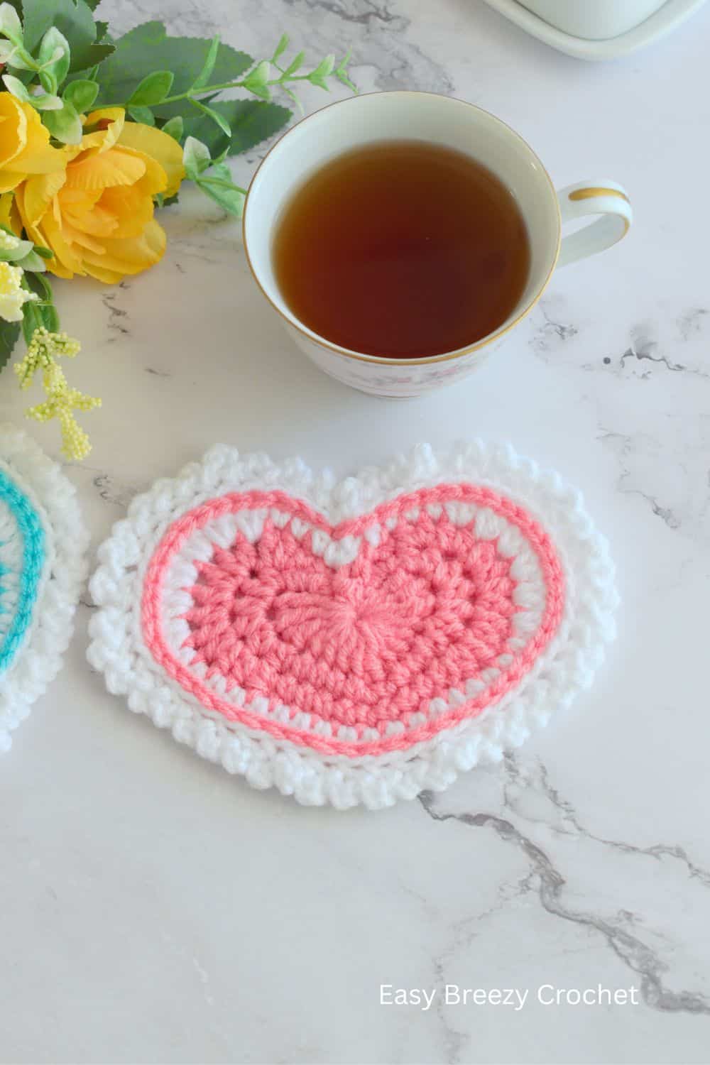 A pink and white crochet coaster with a tea cup.