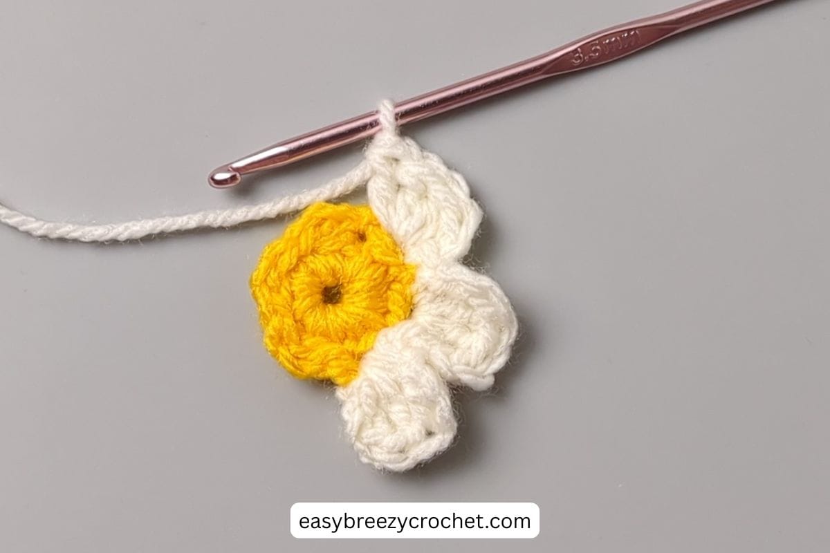 An incomplete crochet flower with a yellow center and cream colored petals.